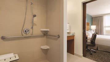 Un baño de hotel con ducha, barras de apoyo, inodoro y lavamanos.