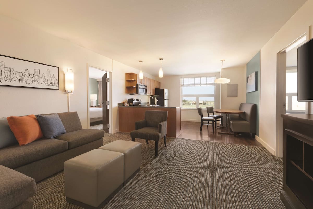 A modern living room with a sofa, ottoman, and a dining area with chairs and a table.