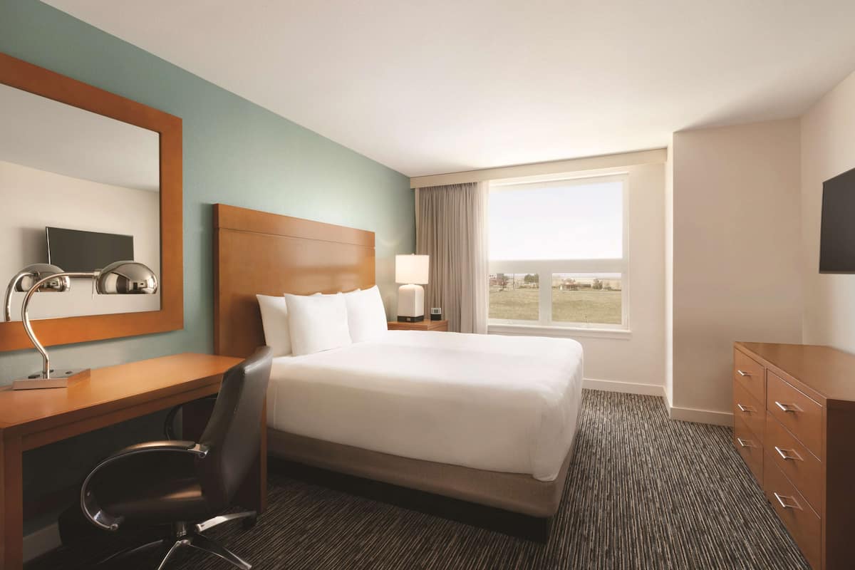 A hotel room with a large bed, a desk with a chair, a TV, a window with a view, and a dresser.