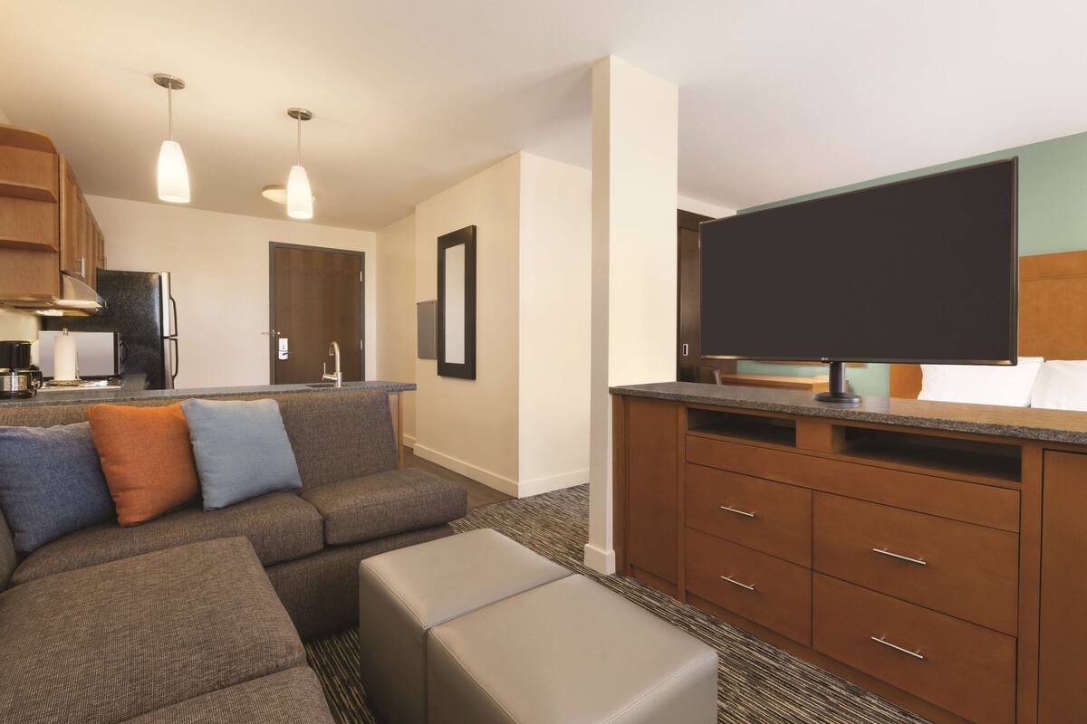A modern hotel room with a living area, kitchenette, and a large flat-screen TV.
