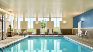 An indoor swimming pool with clear glass walls, lounge chairs, and a view of the outdoors. - Hyatt House Denver Airport (Denver)