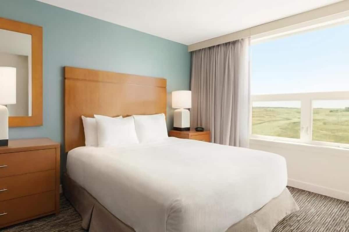 A hotel room with a bed, a dresser, a mirror, two bedside lamps, and a window with a view.