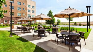 An outdoor patio area with tables and chairs, striped umbrellas, and a barbecue grill. - Hyatt House Denver Airport (Denver)
