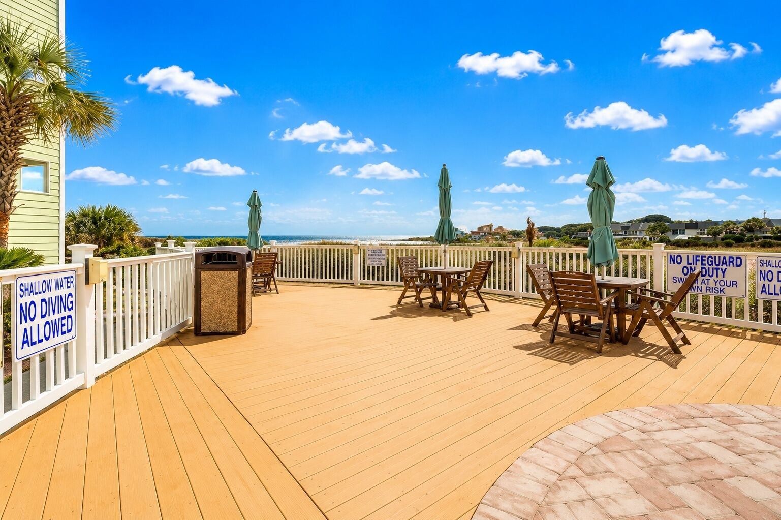 Eine Holzterrasse mit Sitzgelegenheit, einem Mülleimer und Blick auf das Meer.