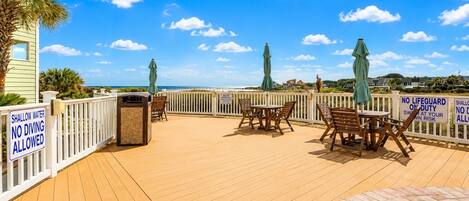 Eine Holzterrasse mit Sitzgelegenheit, einem Mülleimer und Blick auf das Meer.