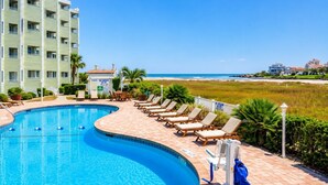 A swimming pool with lounge chairs, a building with balconies, and a view of the beach. - Sands Beach Club (Myrtle Beach)