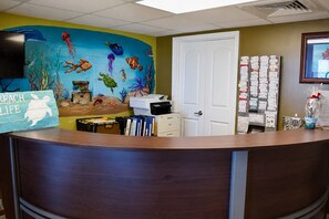 A reception desk with a colorful mural of sea life, a white door, and a bulletin board with cards. - Sands Beach Club (Myrtle Beach)