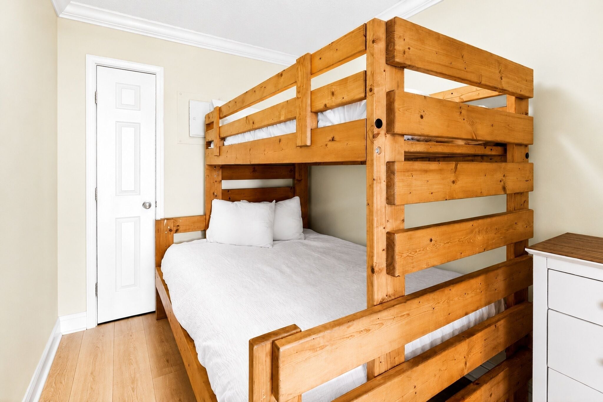 A bunk bed with a wooden frame, a white mattress, and a small bedside table.