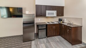 A compact kitchen with dark wooden cabinets, a stainless steel refrigerator, a microwave, and a sink. - Comfort Inn (Dawson Creek)