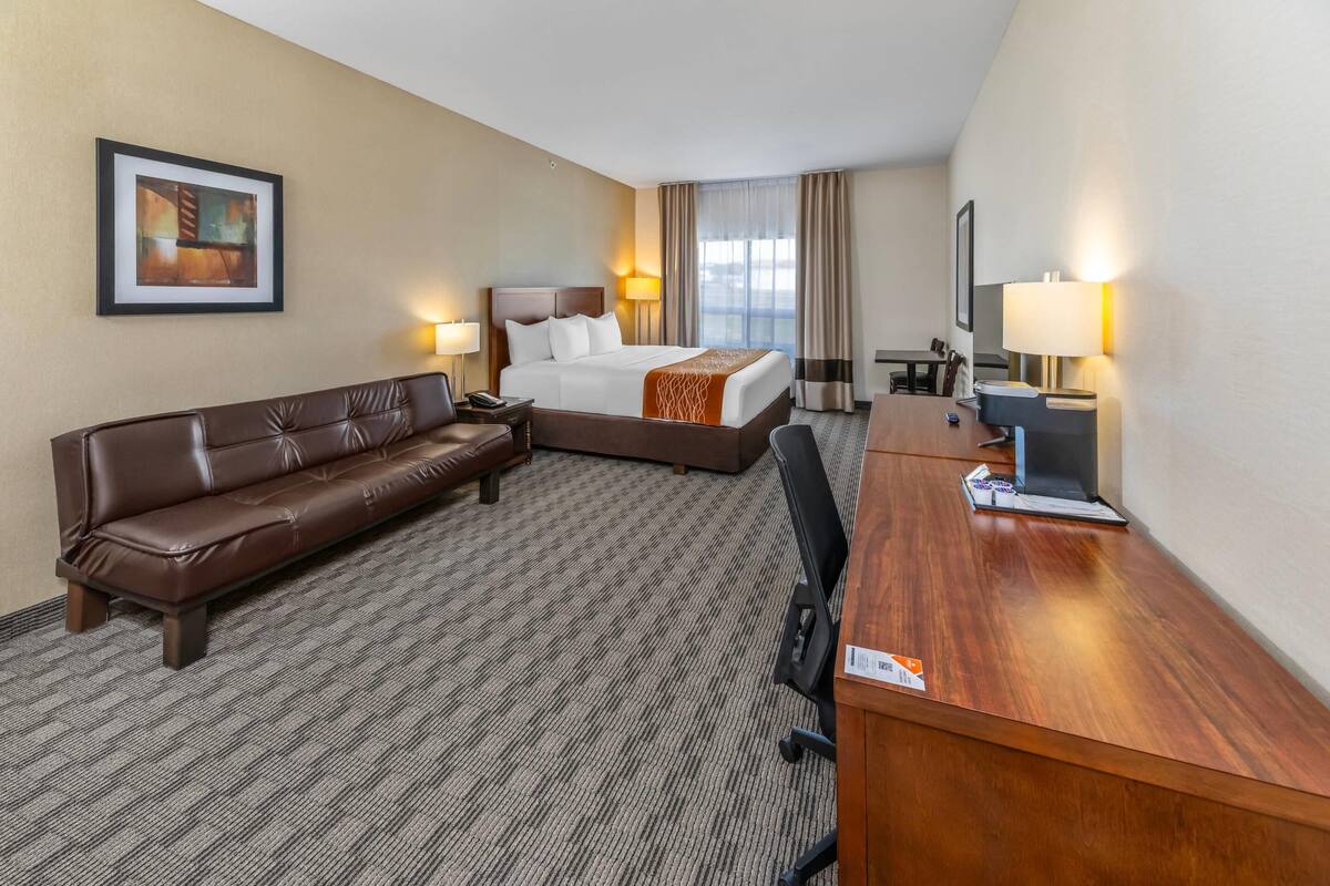 Une chambre d’hôtel avec un lit, un canapé en cuir marron, un bureau en bois et un téléviseur.