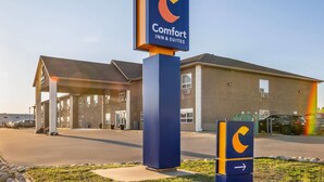 A Comfort Inn & Suites sign with a modern design, a covered parking area, and a building with a flat roof. - Comfort Inn (Dawson Creek)