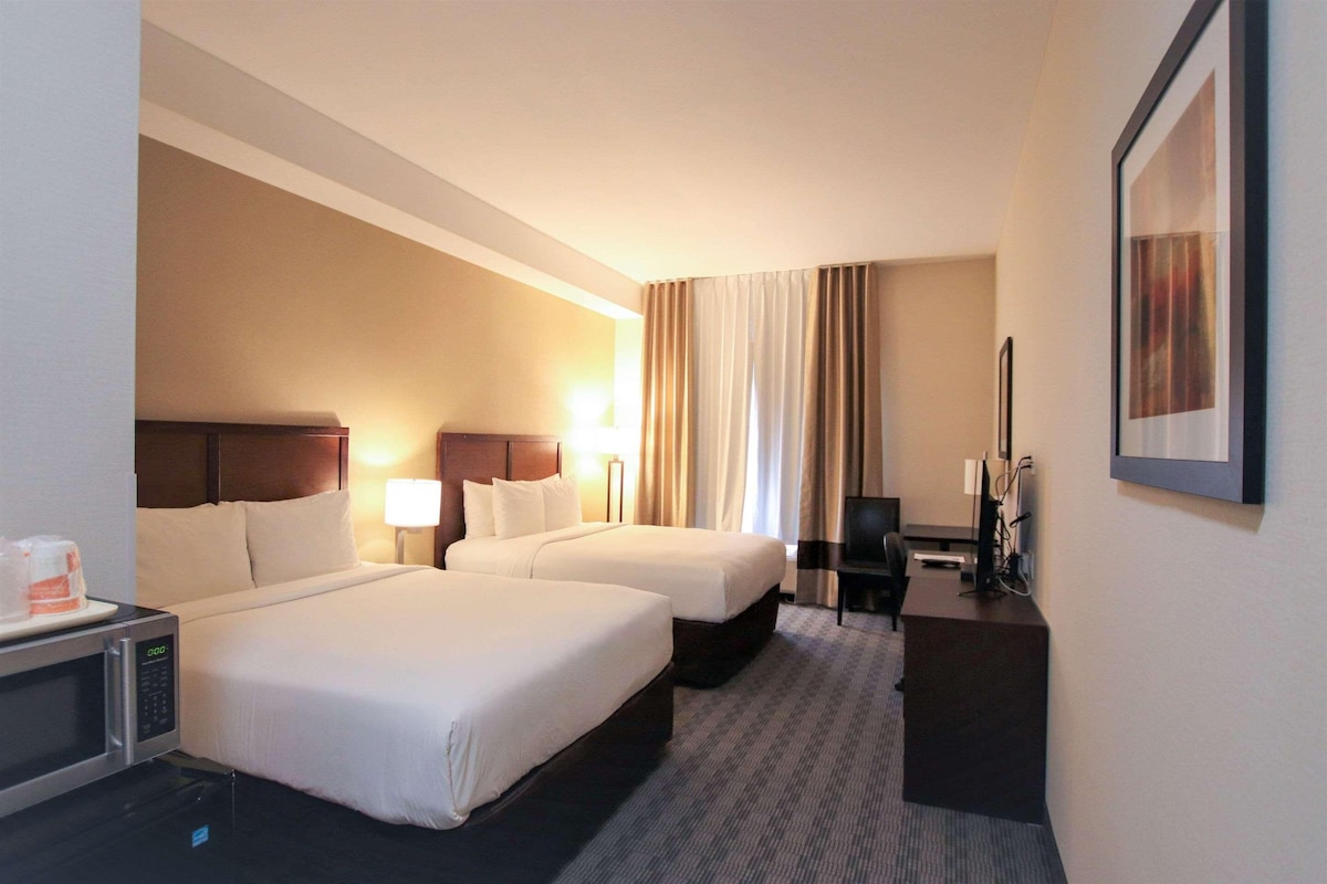 Une chambre d’hôtel avec deux lits, un bureau avec un ordinateur, une télévision et un four à micro-ondes.