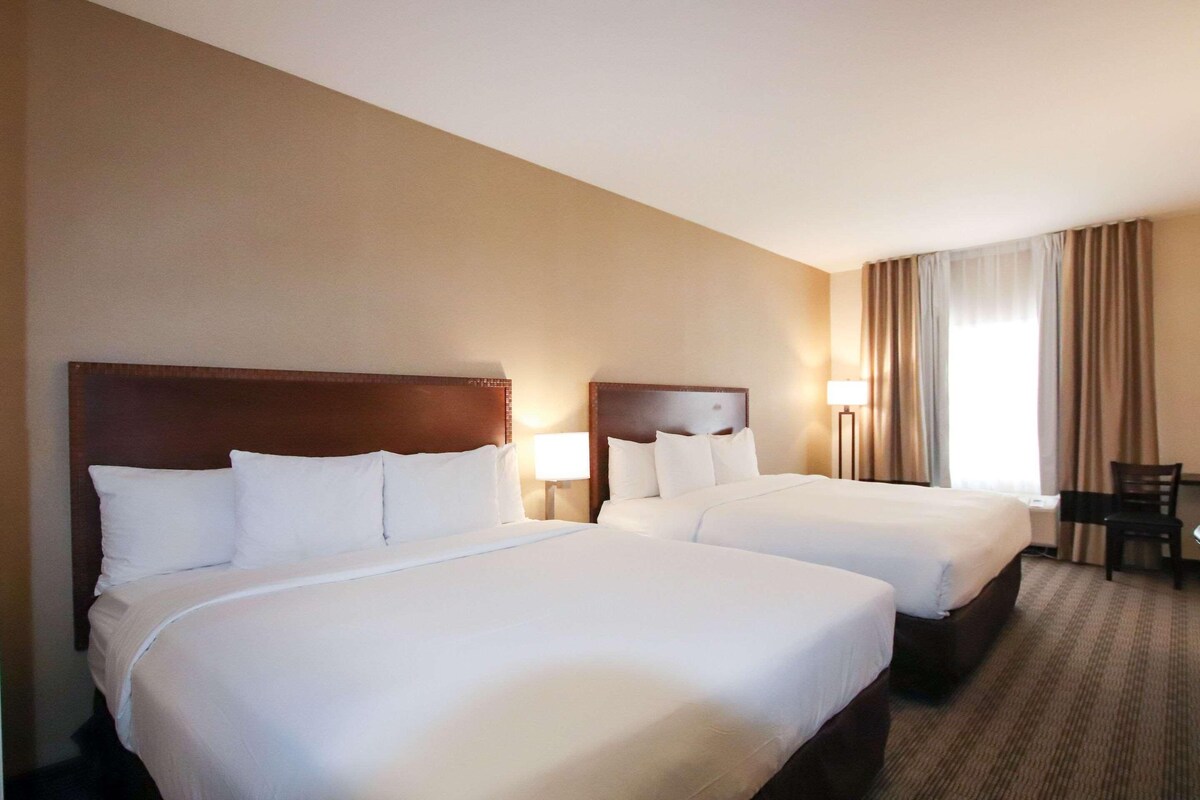 A hotel room with two beds, a desk, and a chair.