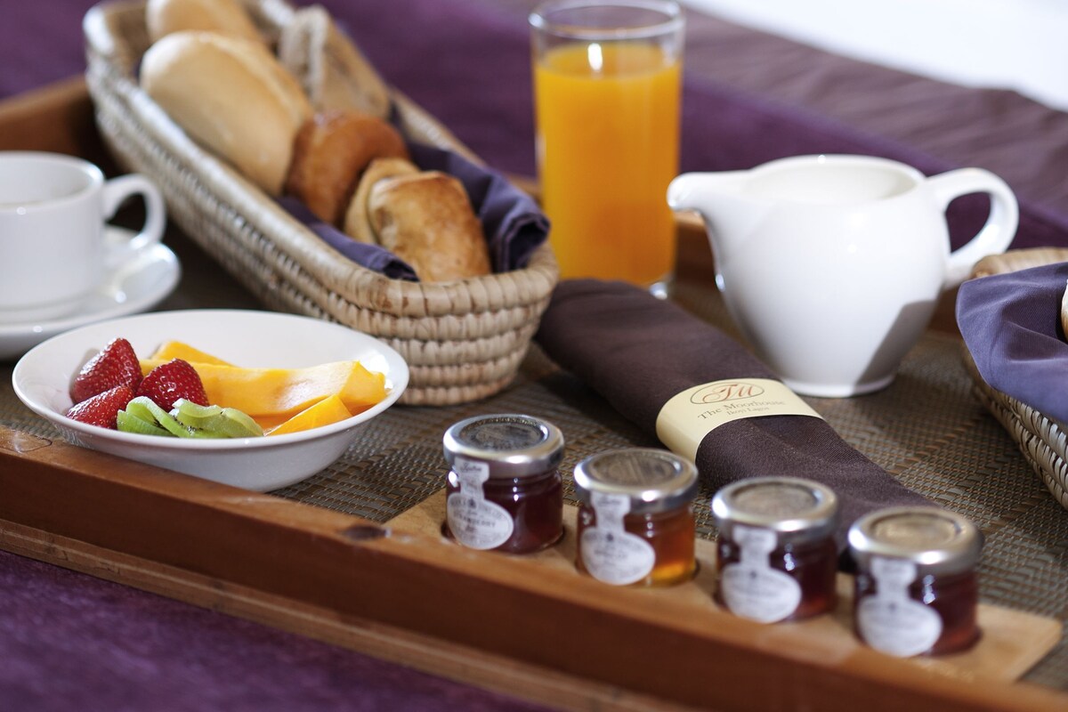 Bandeja de desayuno con pan, fruta, jugo y acompañamientos sobre una cama.
