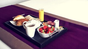 Bandeja de desayuno con cruasanes, un vaso de jugo de naranja, un tazón de fresas y una cafetera.