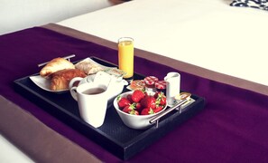 Bandeja de desayuno con cruasanes, un vaso de jugo de naranja, un tazón de fresas y una cafetera.