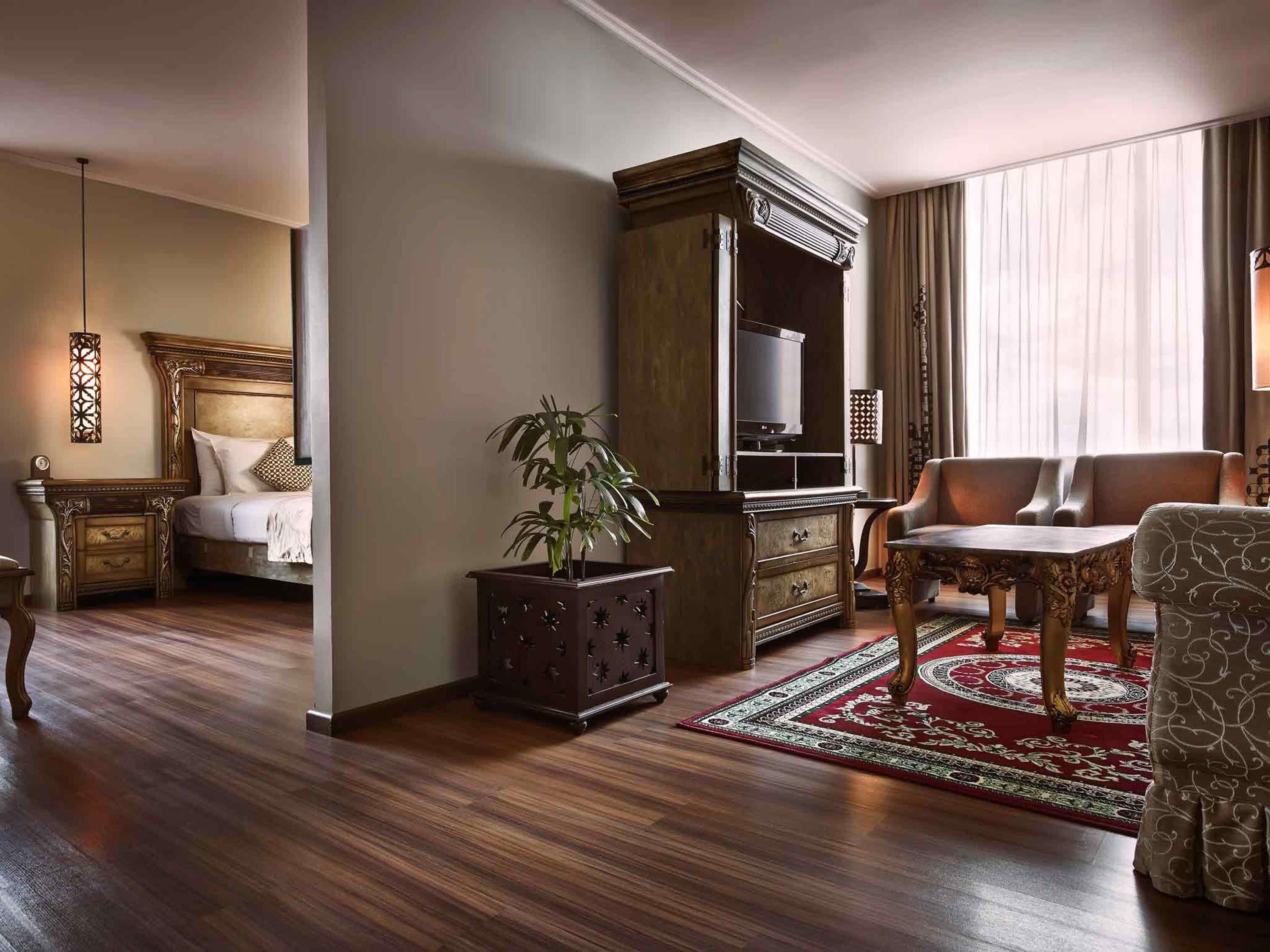 A hotel room with a bed, a desk, a chair, a cabinet, and a plant.