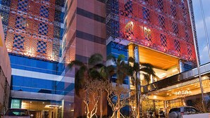 Un edificio moderno con fachada de vidrio y diseño rojo con motivos, y un área de entrada bien iluminada con palmeras.