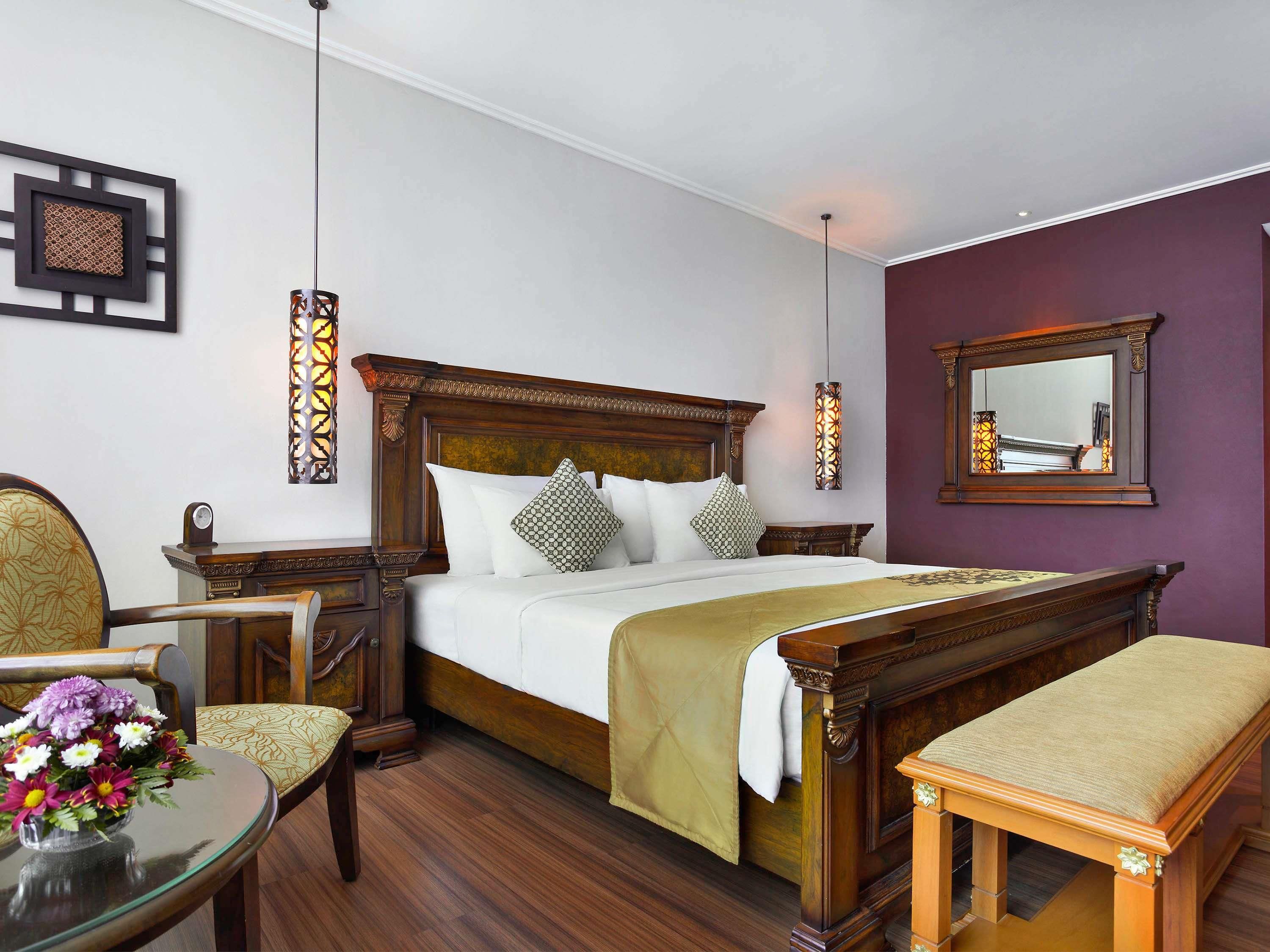 A well-appointed bedroom with a large bed, a bedside table, a chair, a small table with flowers, and a mirror on the wall.