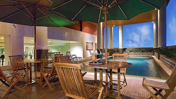 An outdoor pool area with wooden lounge chairs and umbrellas, surrounded by a wooden deck.
