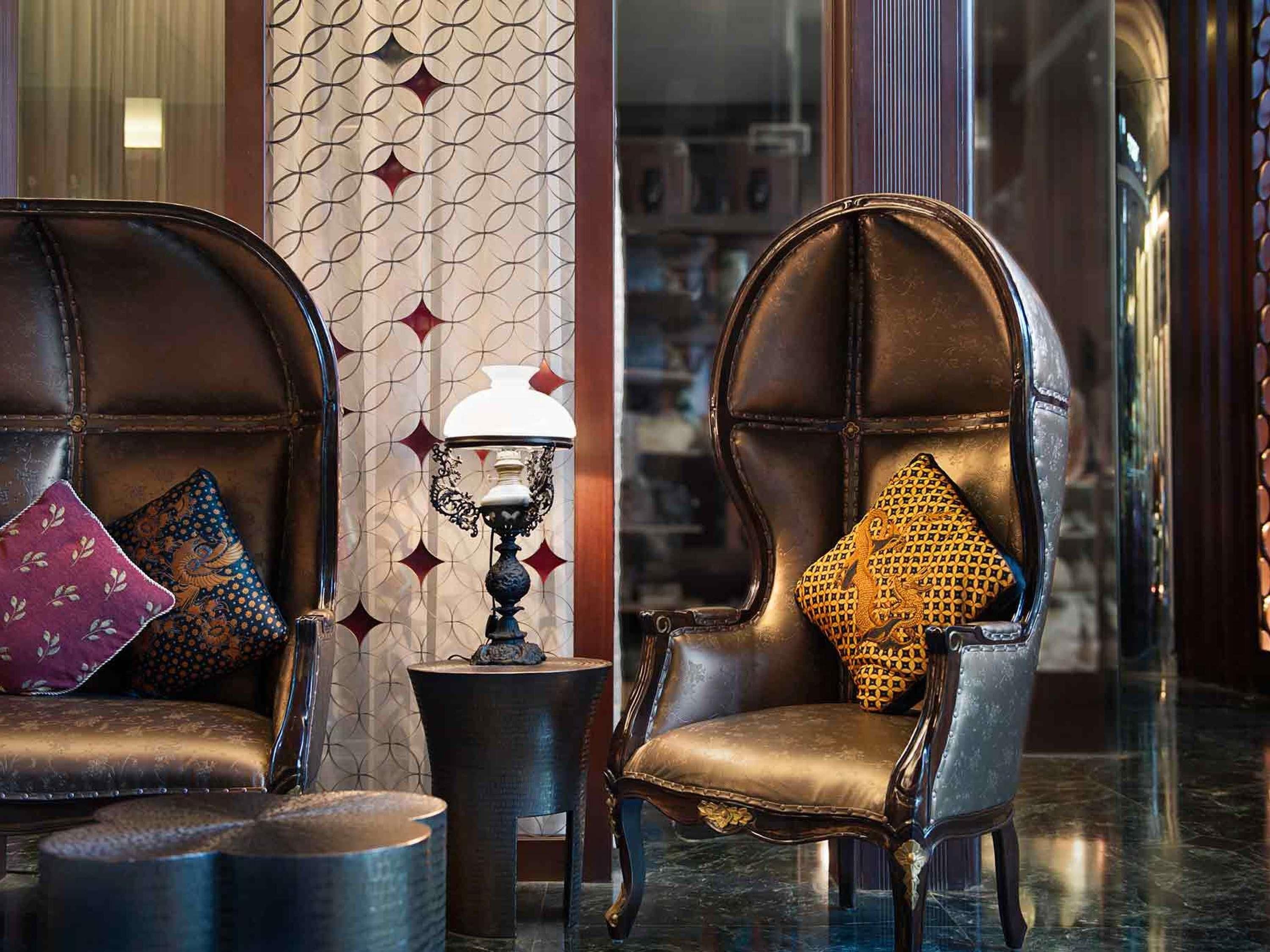 Deux fauteuils en cuir avec des coussins à motifs, une petite table avec une lampe et un mur décoré de motifs.
