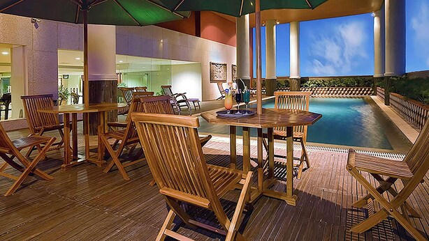 Un área de piscina al aire libre con sillones de madera y sombrillas, rodeada por una terraza de madera.