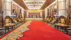 Un amplio vestíbulo con alfombra roja, candelabros ornamentados y una mesa de recepción.