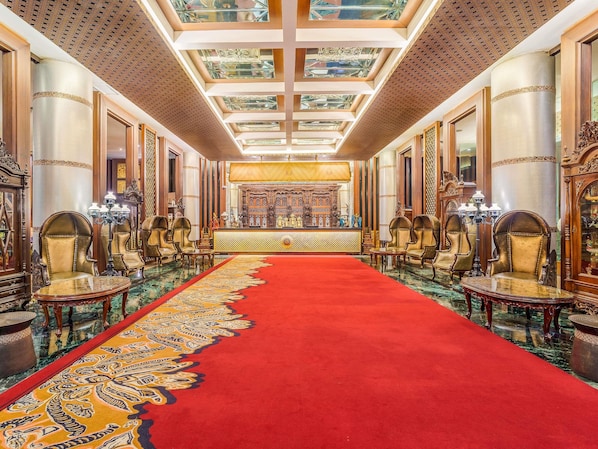 Un amplio vestíbulo con alfombra roja, candelabros ornamentados y una mesa de recepción.