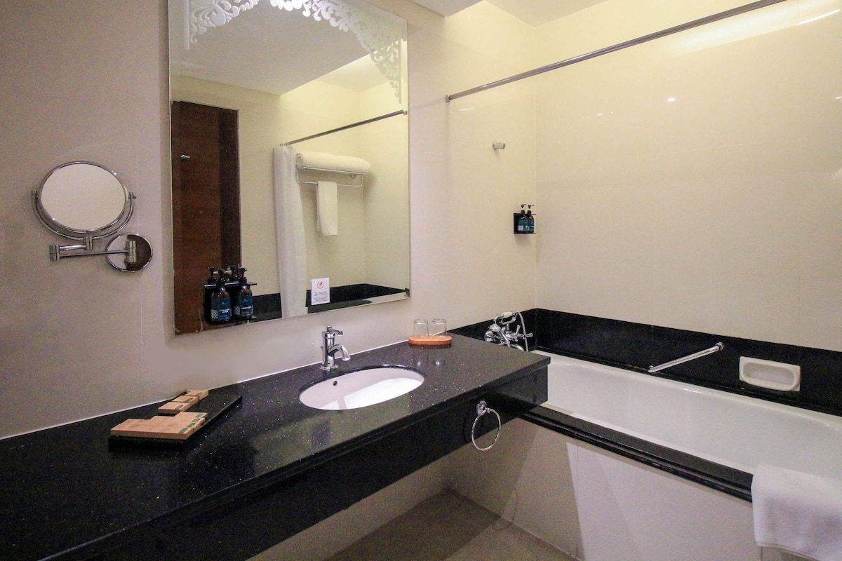 Un baño moderno con encimera negra, lavabo blanco, espejo grande y bañera blanca.
