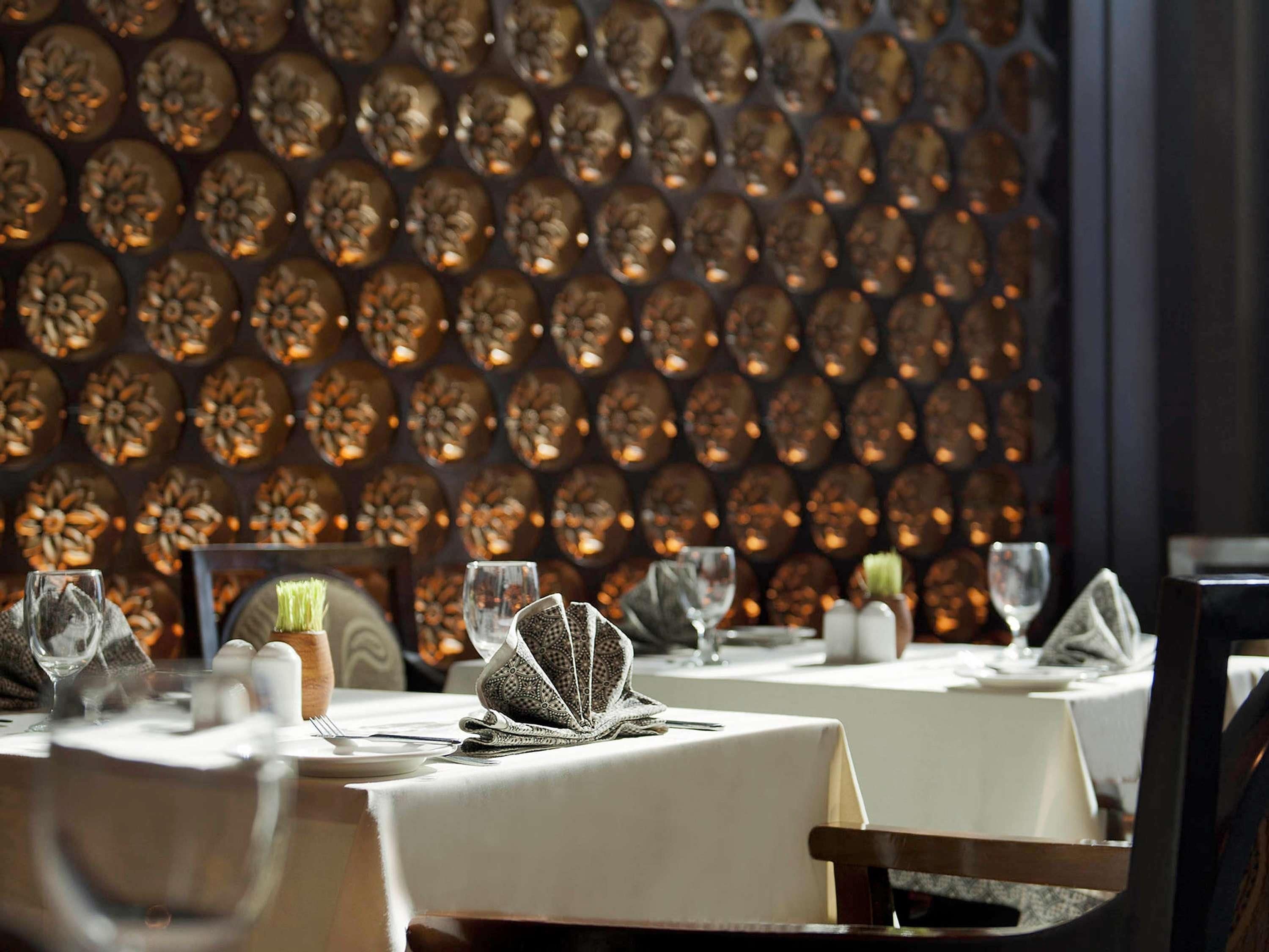 L’intérieur d’un restaurant, avec des tables dressées pour le service, un mur à motifs en arrière-plan, et des salières et des poivrières sur les tables.