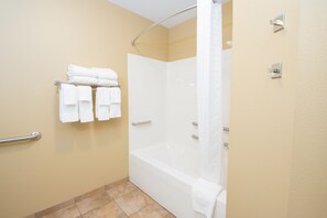 Une salle de bain d’hôtel équipée d’une baignoire, d’une douche et d’un porte-serviettes avec des serviettes pliées.