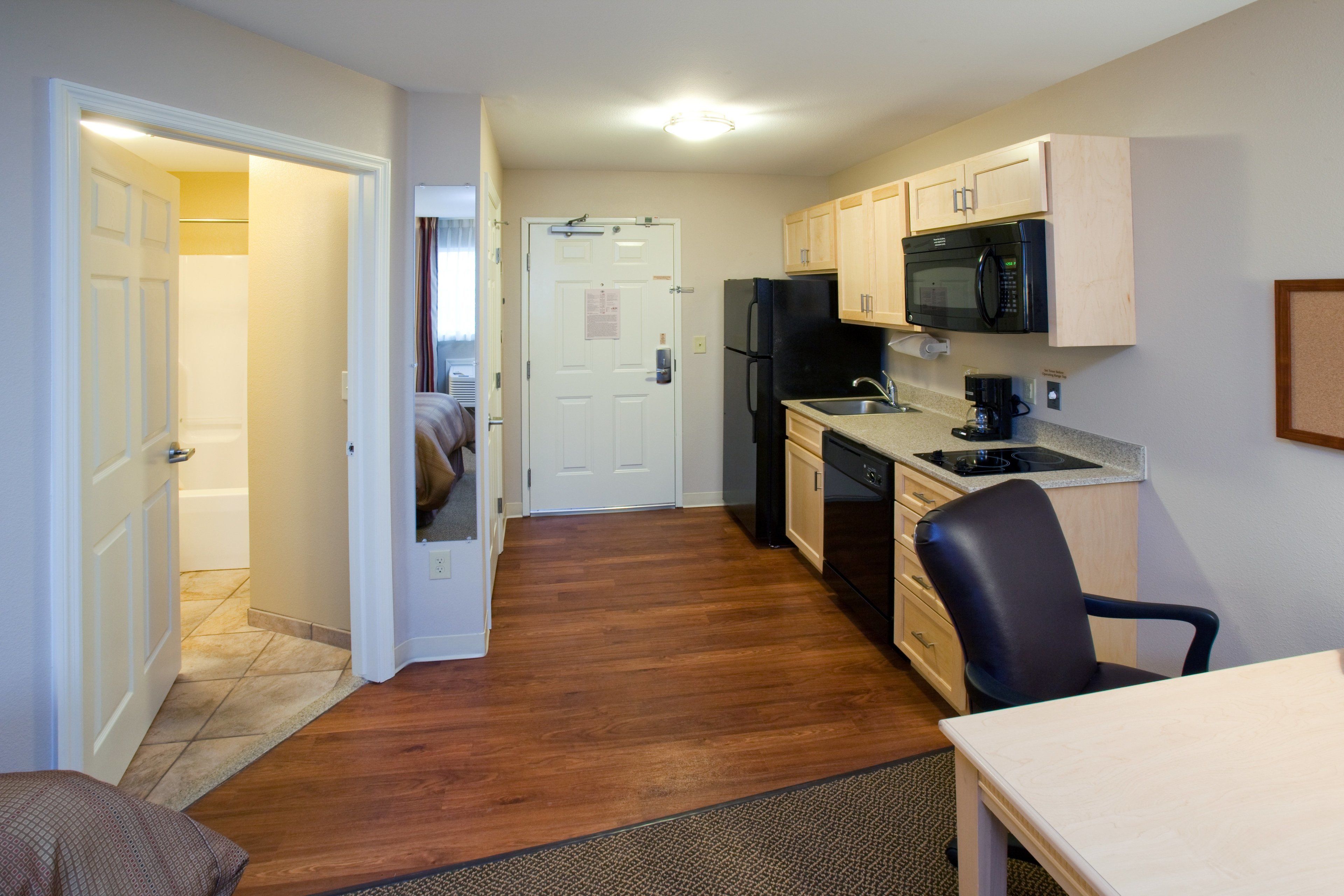 A compact kitchen with wooden cabinets, a black refrigerator, a microwave, and a coffee maker.