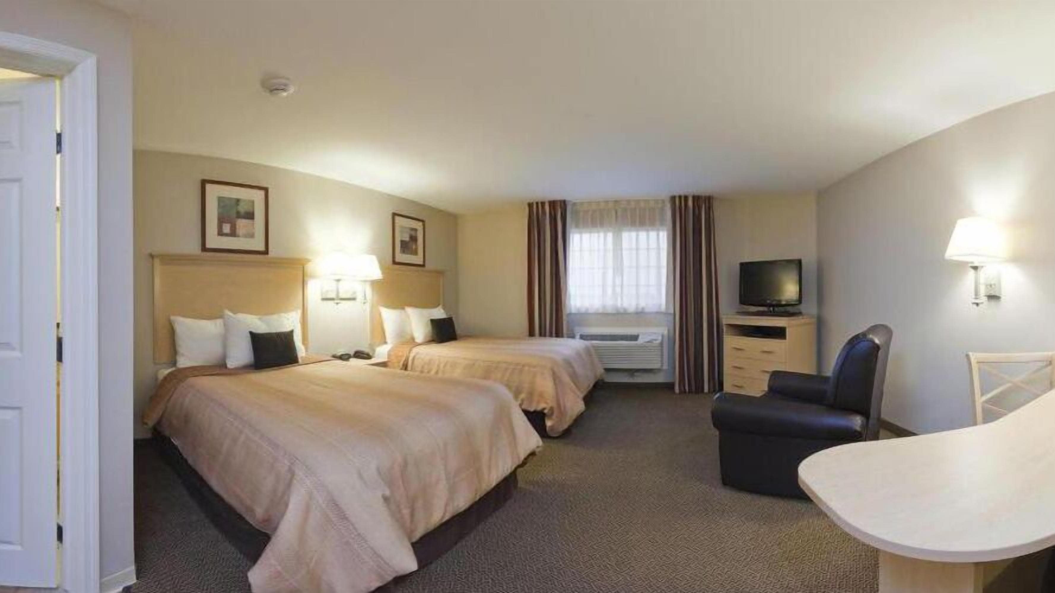 A hotel room with two beds, a TV, a desk, and a chair.