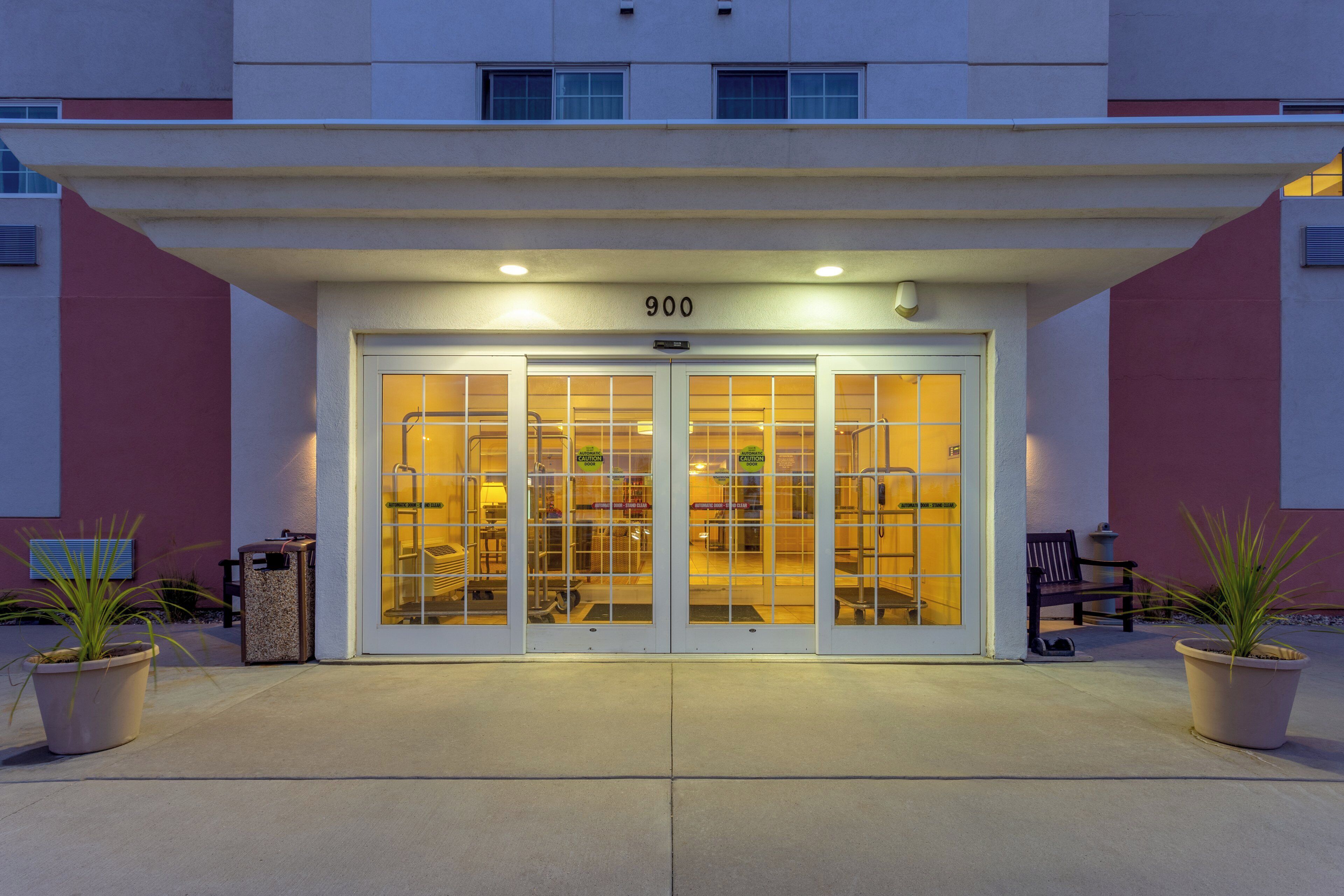 A hotel entrance with a glass door, a number '900' above the door, and potted plants on either side.