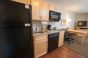 Una cocina compacta con armarios de madera, un refrigerador negro, un microondas, una cafetera y un lavavajillas.