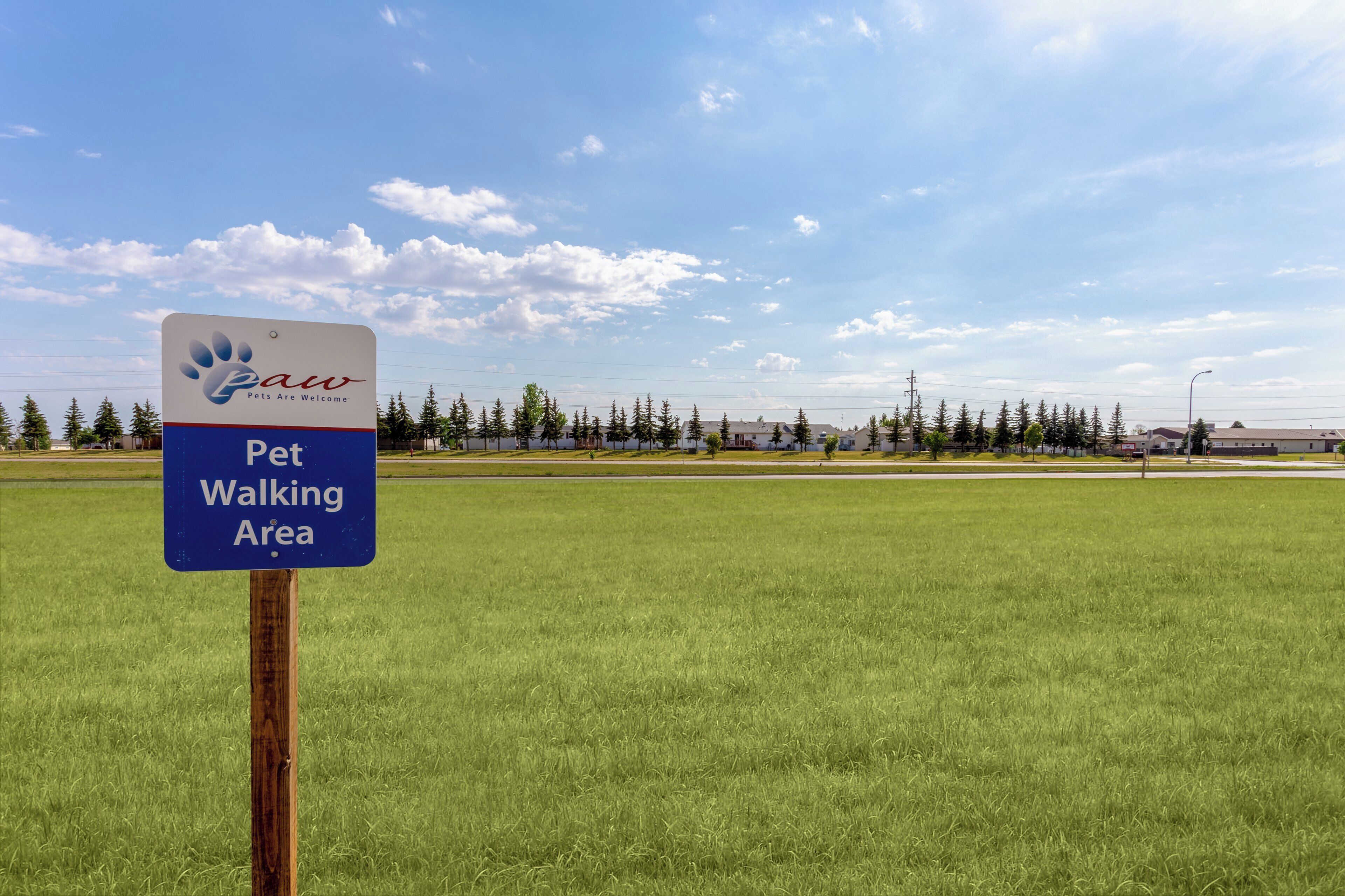 A sign indicating a pet walking area with a clear sky and a grassy field in the background.