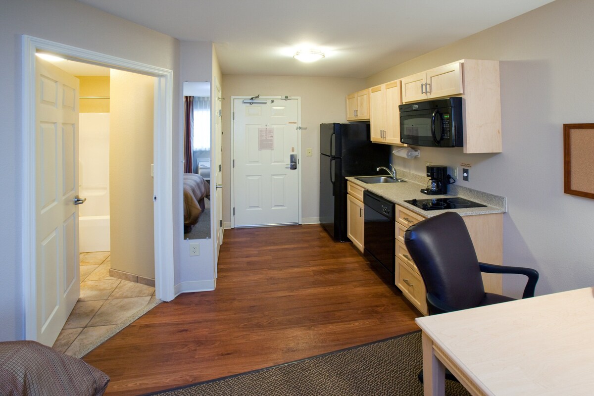 A compact kitchen with wooden cabinets, a refrigerator, a microwave, and a coffee maker.