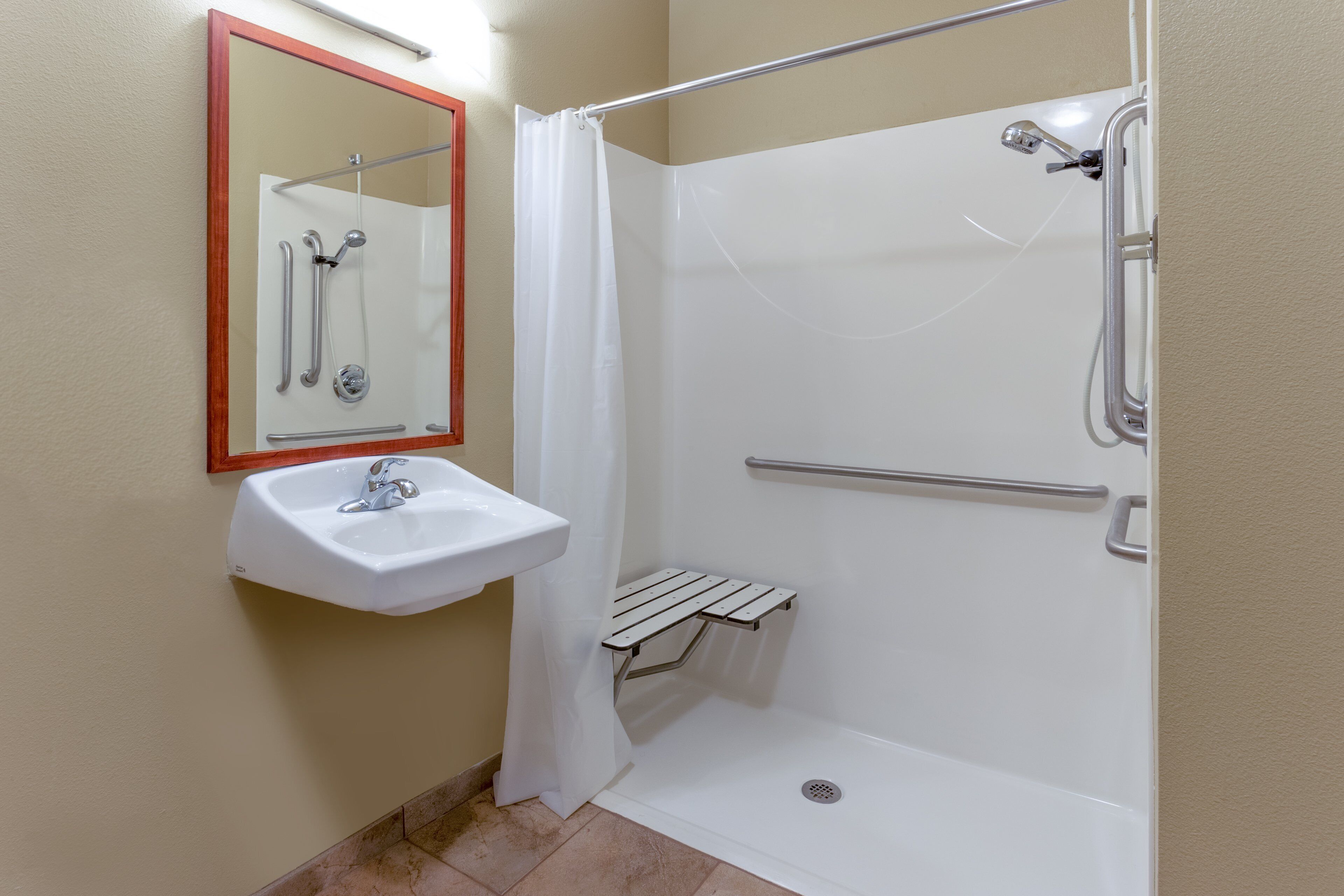 Un baño con lavamanos blanco, un espejo, ducha con puerta de cristal y barra de apoyo.