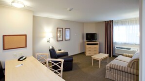 Ett hotellrum med ett skrivbord, en stol, en soffa, en tv, ett litet bord och en luftkonditioneringsanläggning.
