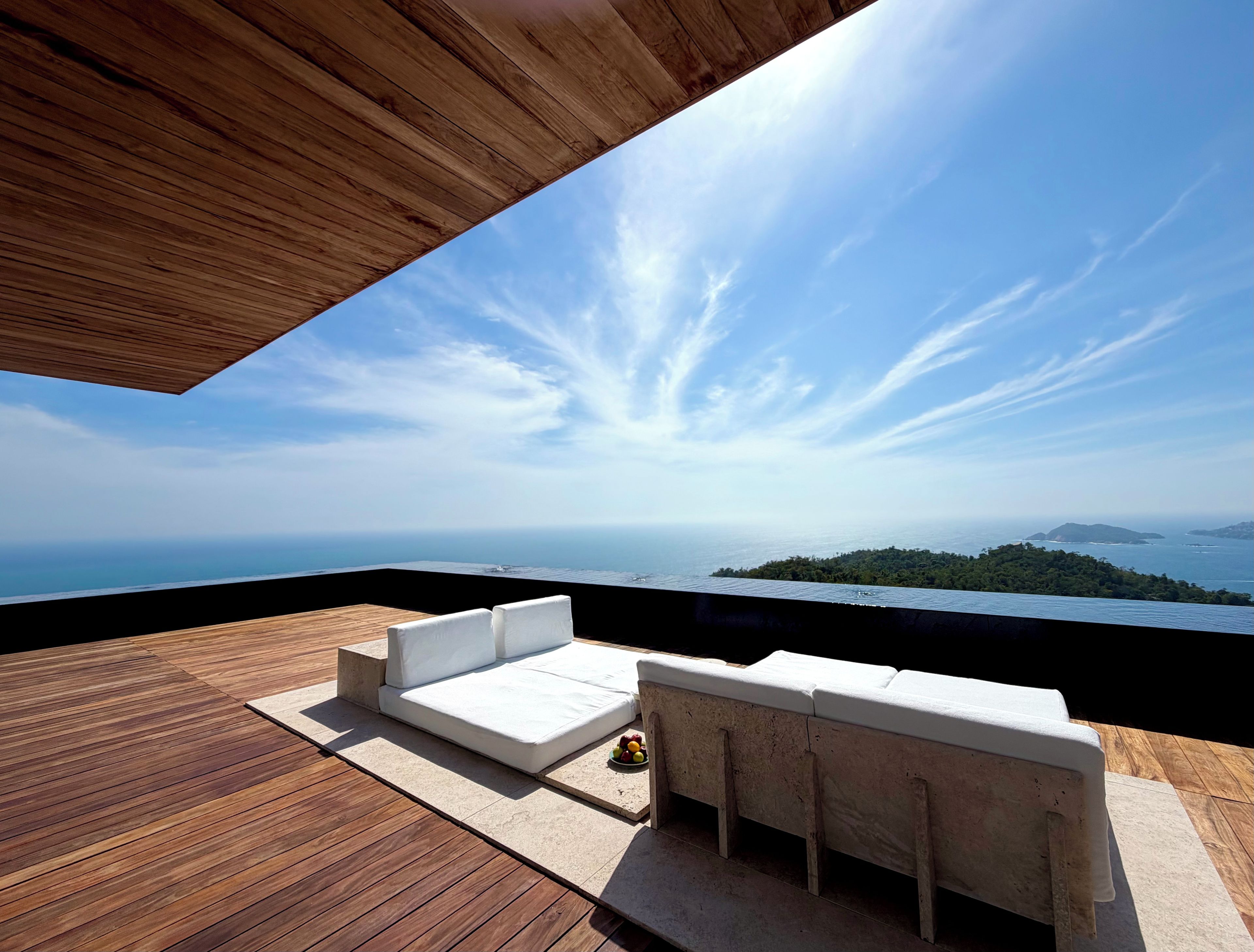 A wooden deck with a white sofa and a small table, overlooking a coastal landscape.