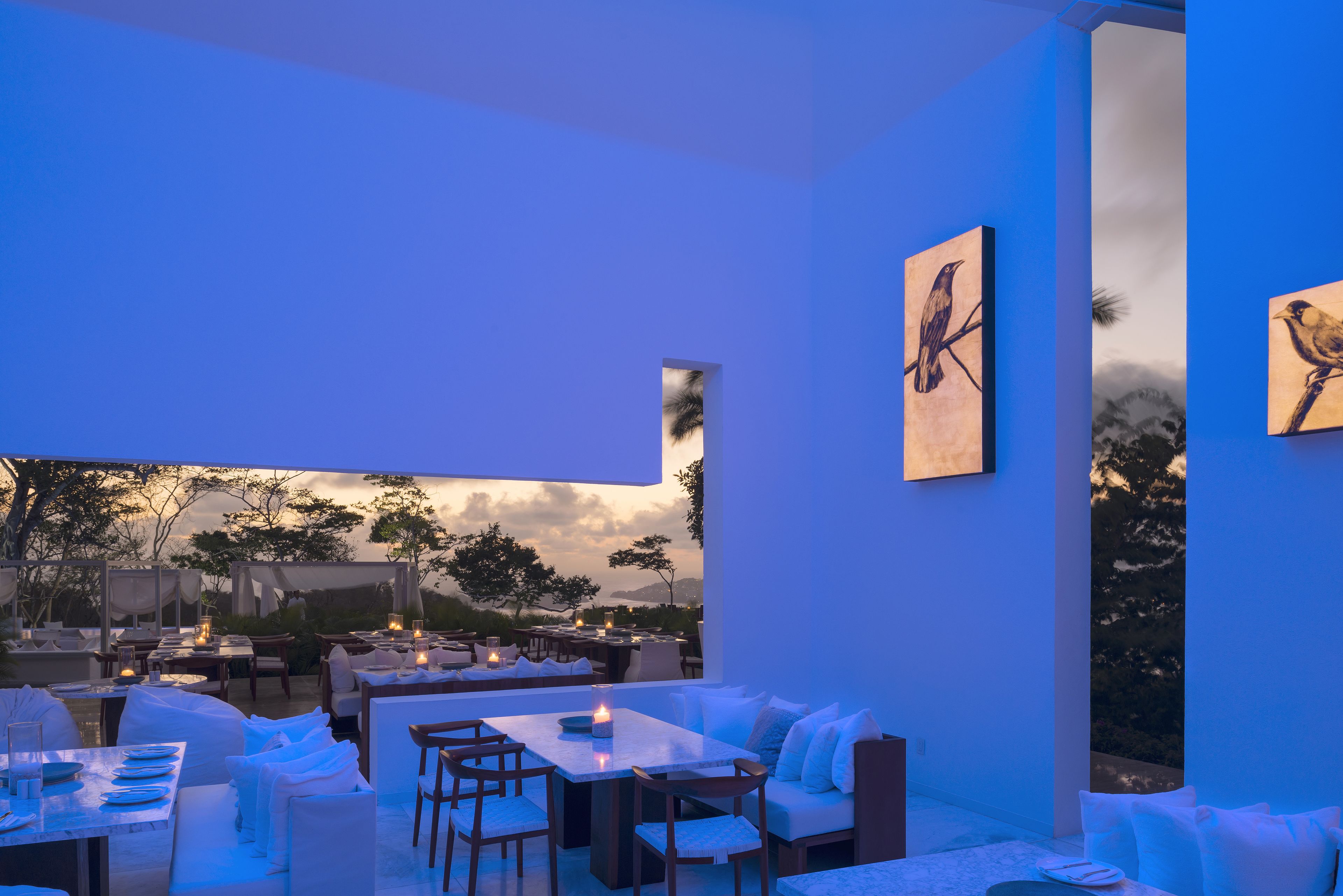 Un espacio de comedor al aire libre con mesas y sillas, vistas del paisaje y obras de arte en las paredes.