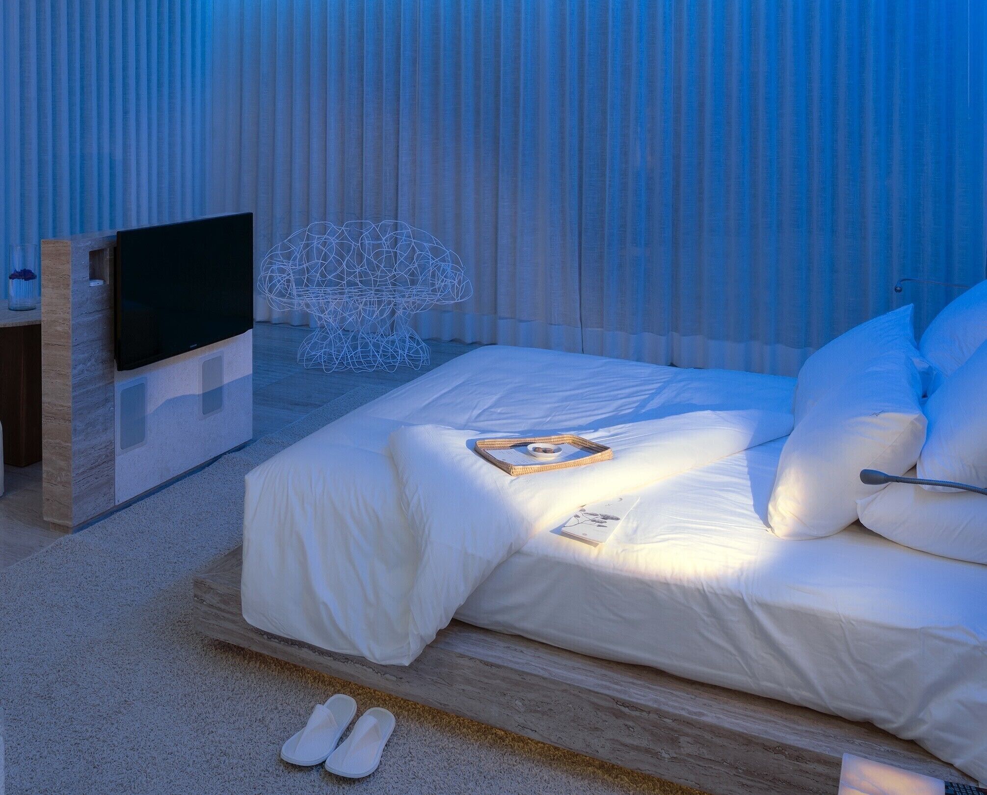 A modern bedroom with a bed, a flat-screen TV, and a decorative wire sculpture.