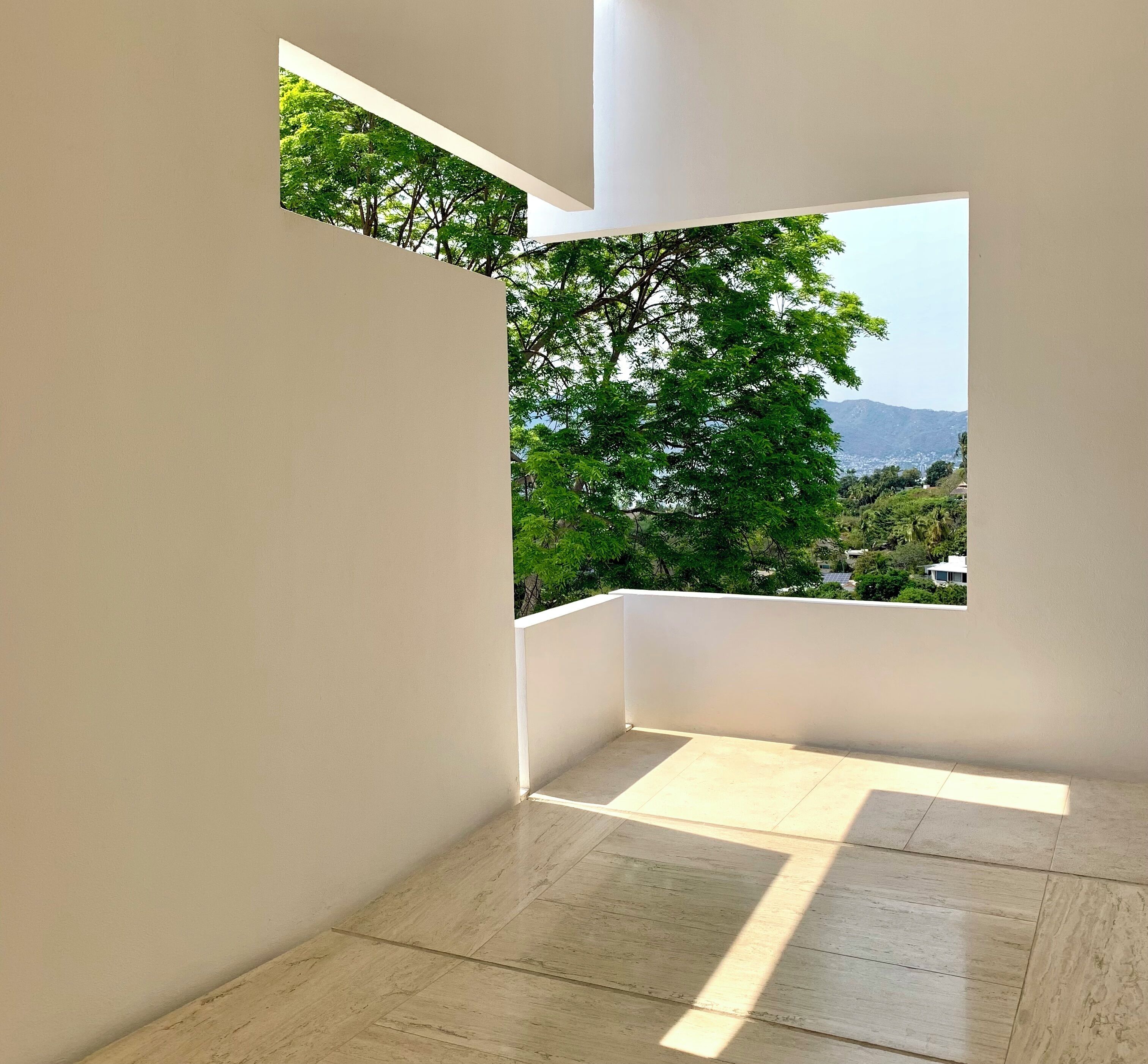 Una habitación moderna y minimalista con un amplio ventanal que ofrece vistas a vegetación exuberante y colinas distantes.