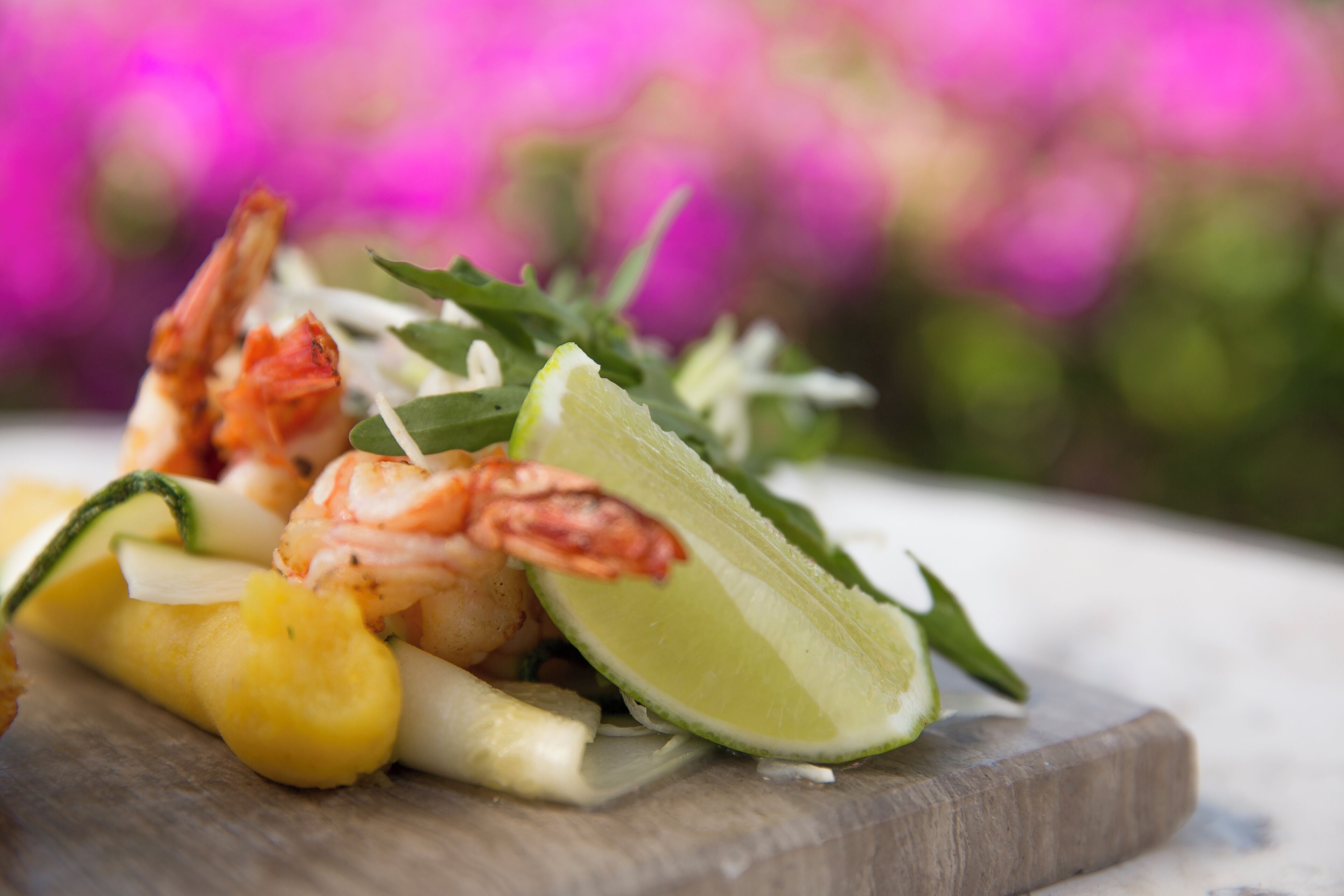 A wooden board with shrimp, pineapple, and lime.