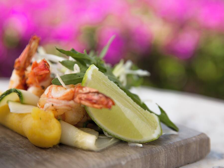 A wooden board with shrimp, pineapple, and lime.