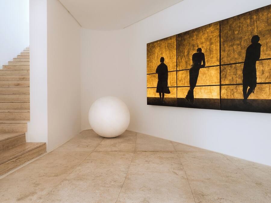 A modern interior with a staircase, a large white spherical sculpture, and a wall with silhouettes of people.