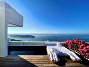 A balcony with a wooden floor, a bed with white linens, and a view of the sea. - Encanto Acapulco (Acapulco)
