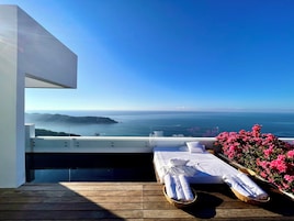 Un balcón con suelo de madera, una cama con sábanas blancas y vista al mar.