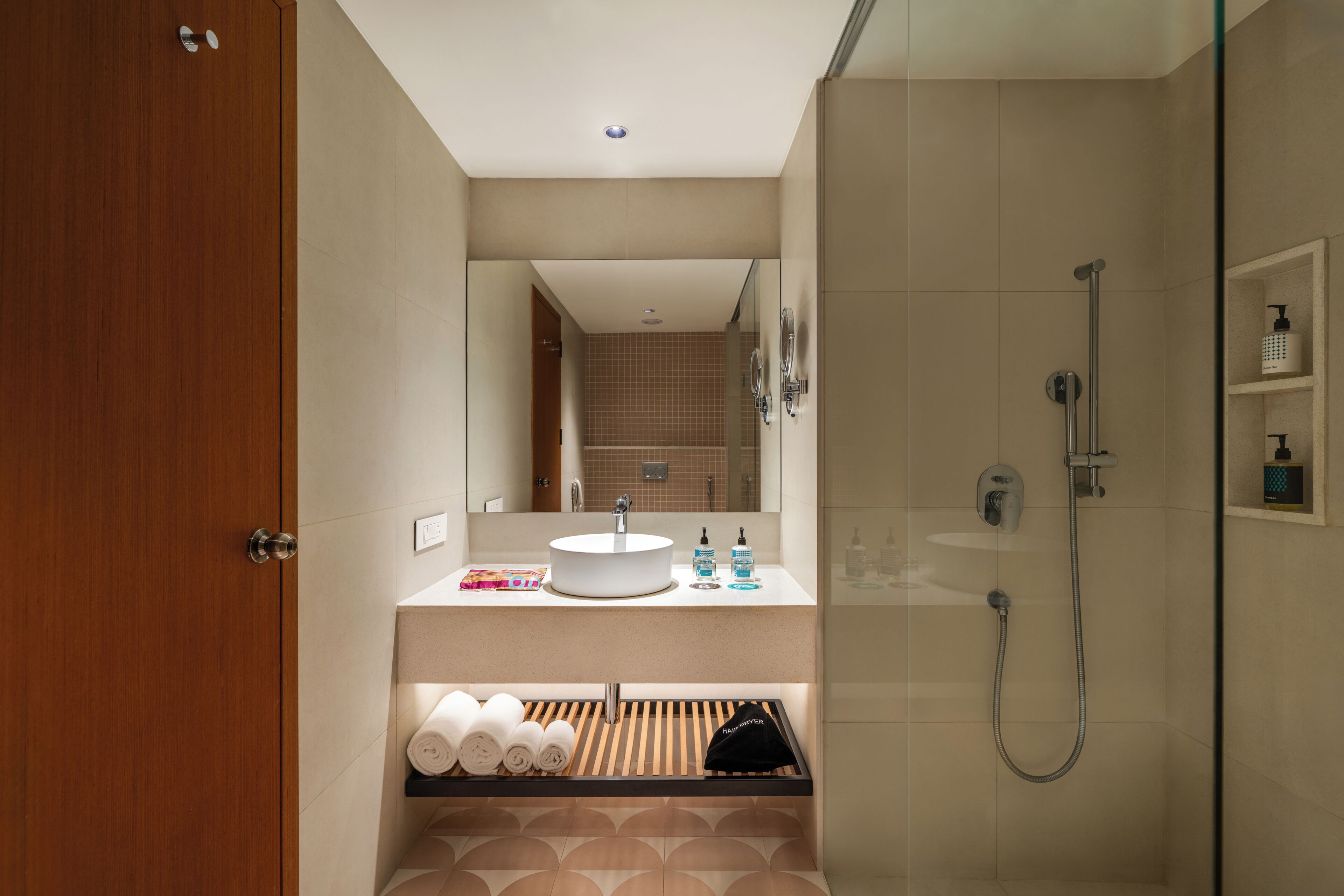 Ein modernes Badezimmer mit Holztür, Waschbecken mit Spiegel, Dusche und ordentlich zusammengefalteten Handtüchern.