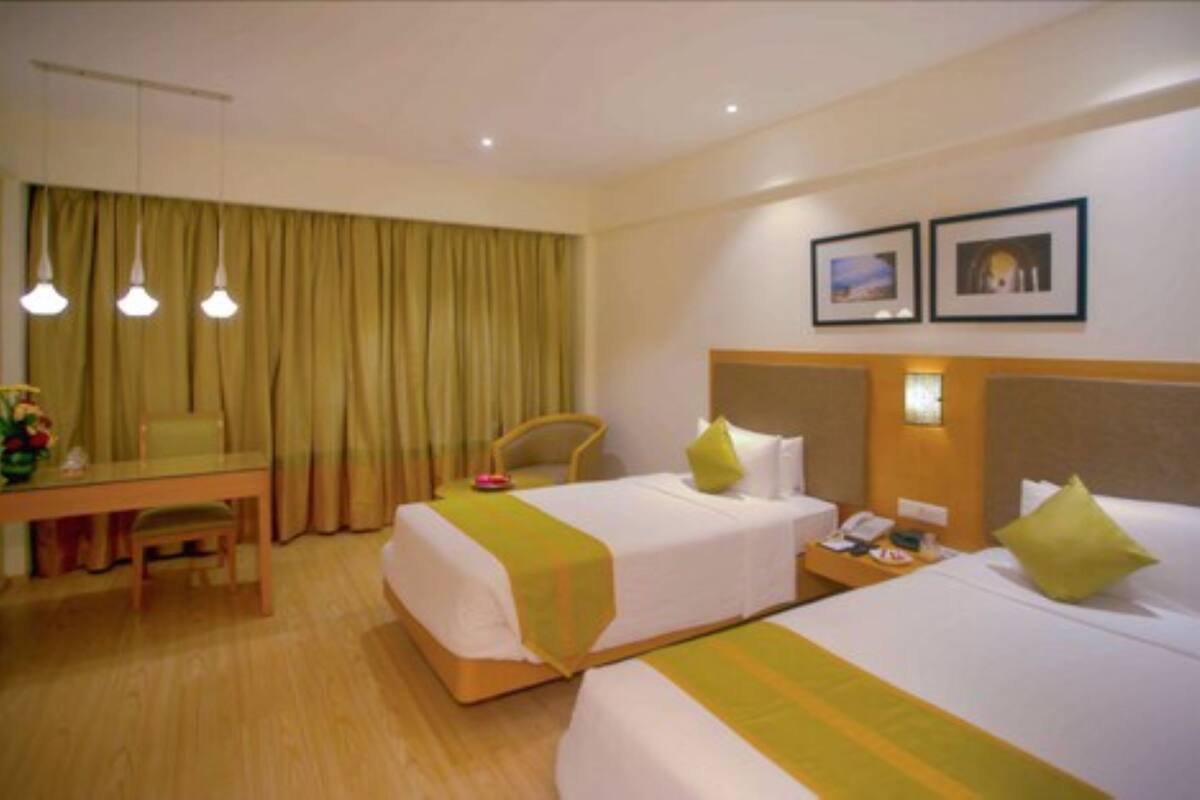 Habitación de hotel con dos camas, un escritorio, una silla y un ventanal con cortinas.